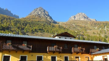Ein gelbes Gebäude mit hölzernen Balkonen, einer Holzterrasse und einem Berg im Hintergrund.