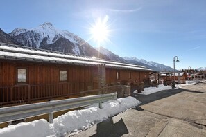 Un bâtiment en bois avec une rambarde en métal, de la neige au sol et des montagnes en arrière-plan.
