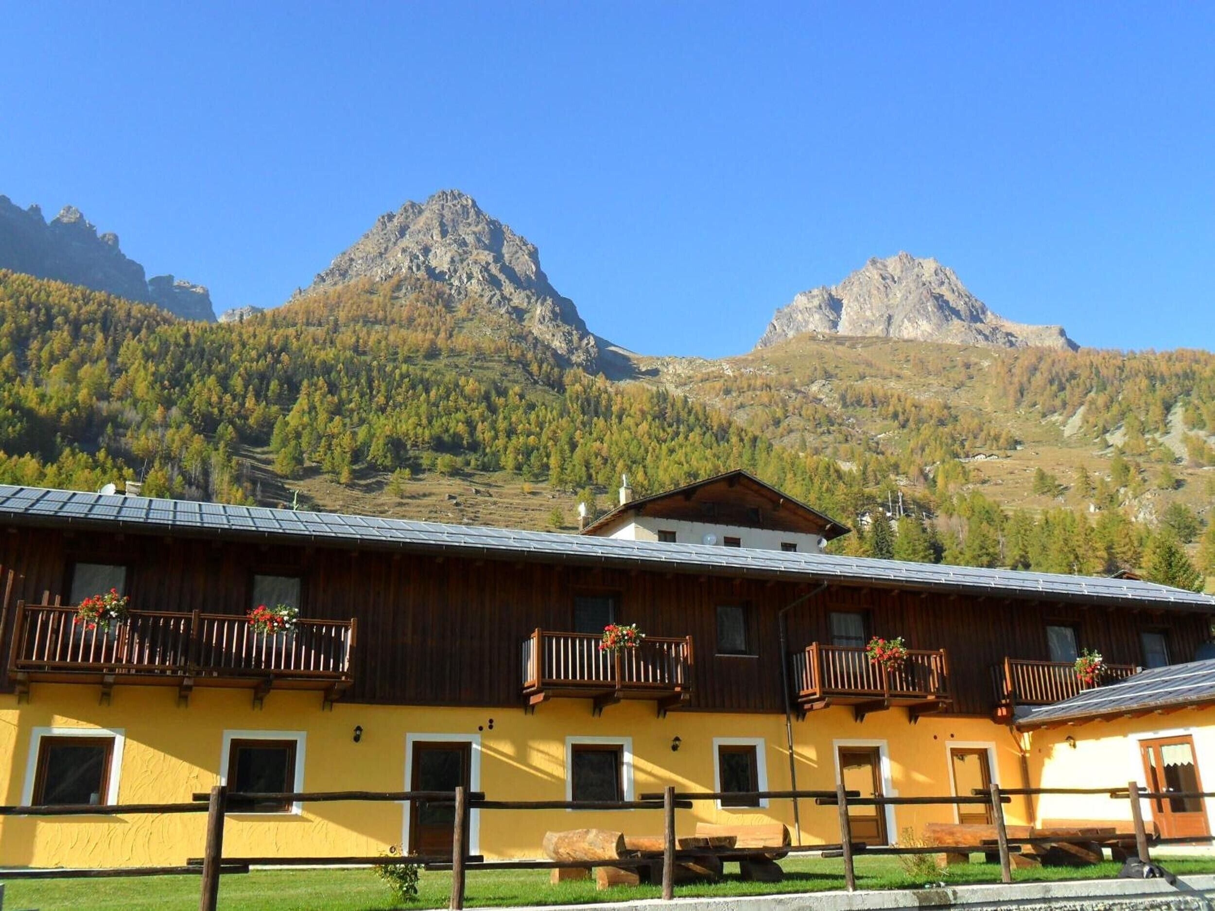 Ein gelbes Gebäude mit hölzernen Balkonen, einer Holzterrasse und einem Berg im Hintergrund.