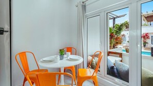 Ein Zimmer mit einem weißen Tisch und vier orangenen Stühlen, eine Schiebetür zu einem Außenbereich mit Pool und Pflanzen.