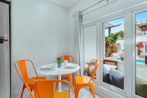 A room with a white table and four orange chairs, a sliding glass door leading to an outdoor area with a pool and plants. - The Shoco 1Br-1Ba near Beach Eva Boutique&Spa (Savaneta)
