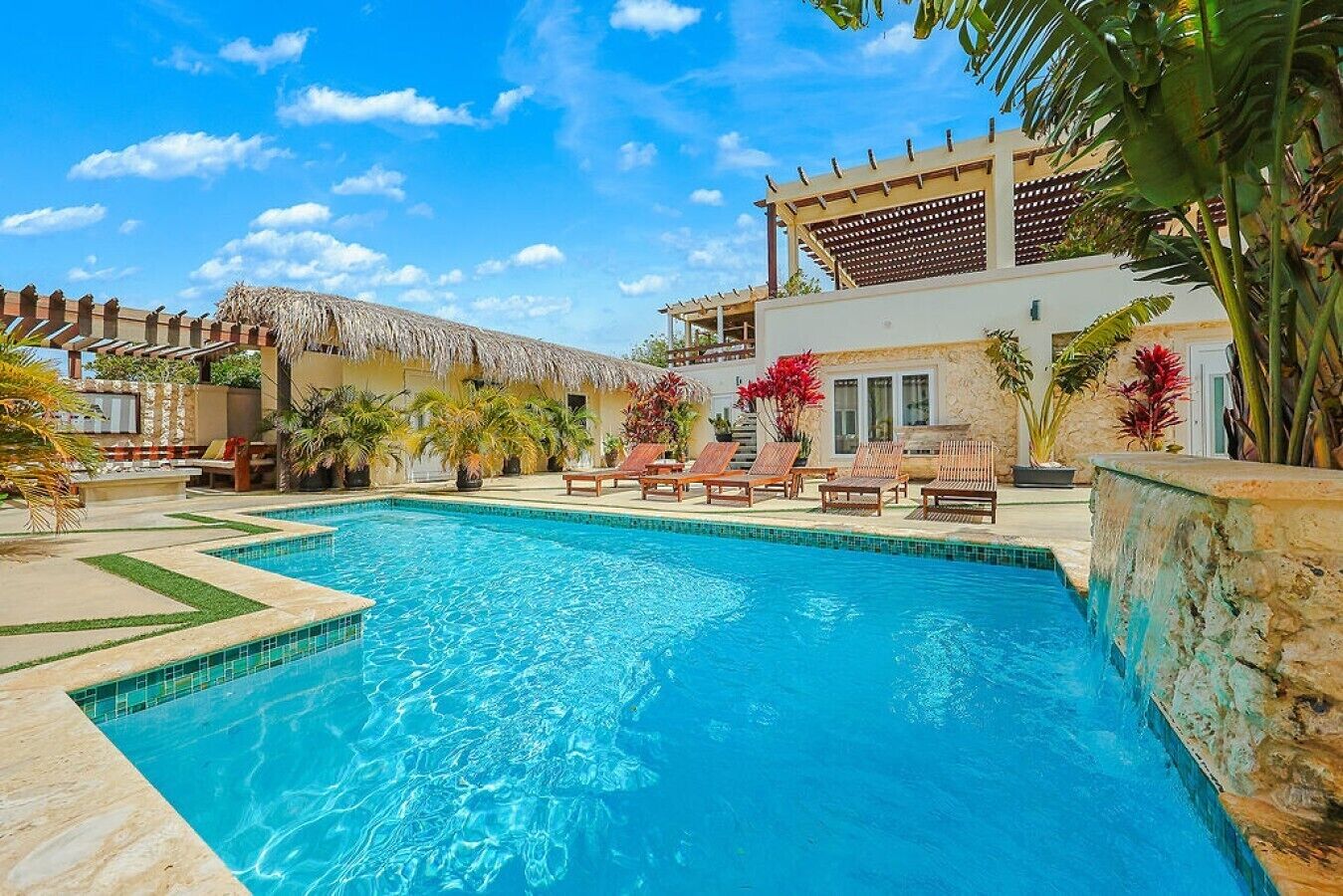Una piscina con sillas de descanso y plantas tropicales.