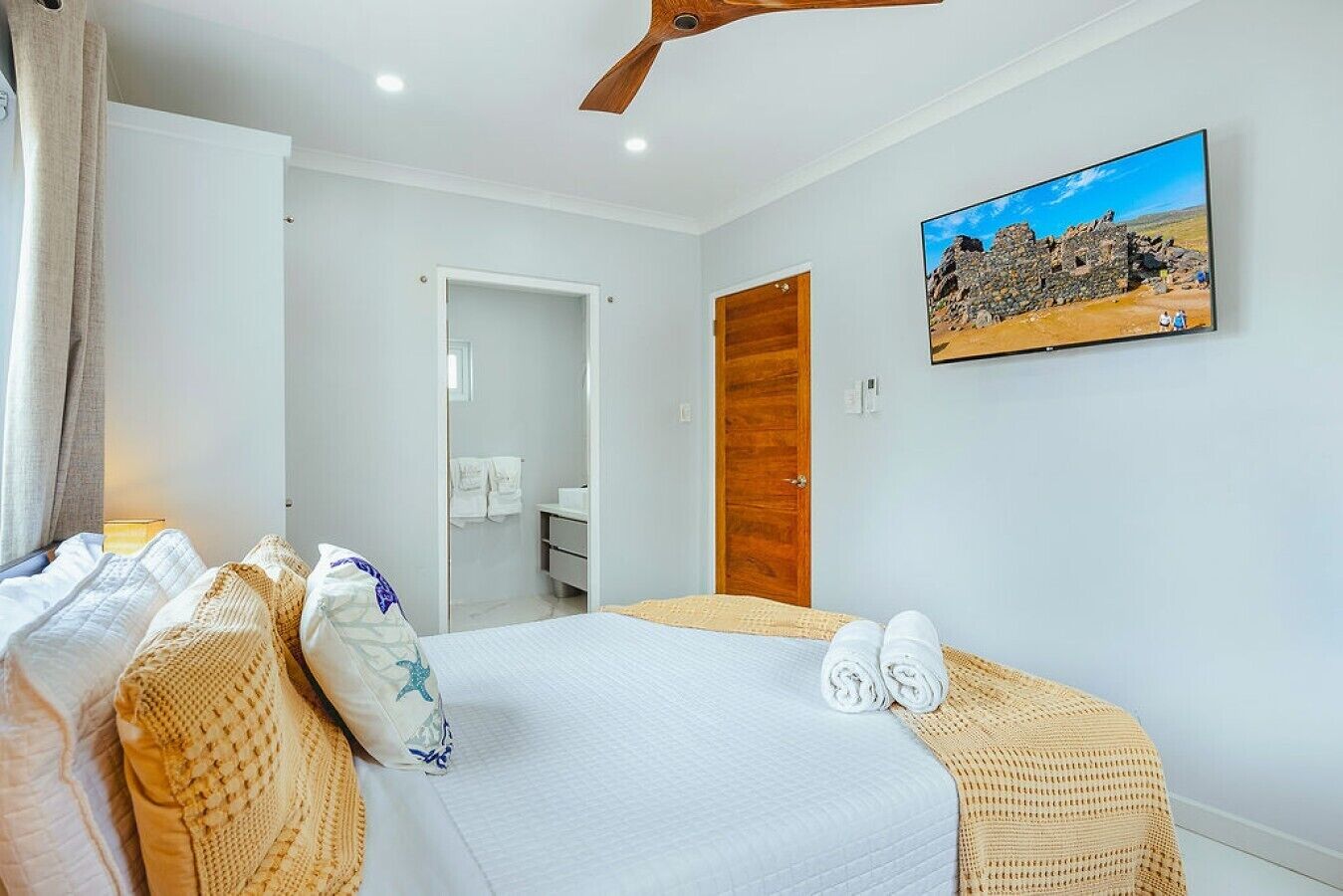 Une chambre d’hôtel avec un lit, une porte en bois, un tableau et une salle de bain visible à travers une porte ouverte.