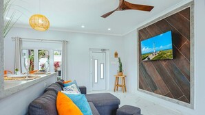 Ein modernes Wohnzimmer mit einer Couch, einem an der Wand montierten Fernseher und einem Deckenventilator.