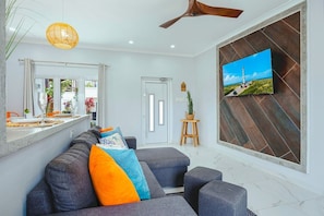 A modern living room with a sofa, a television mounted on the wall, and a ceiling fan. - The Shoco 1Br-1Ba near Beach Eva Boutique&Spa (Savaneta)