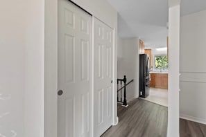 A hallway with a white door, a black railing, and a kitchen area in the background.