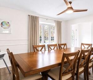 A dining room with a wooden table and chairs, a ceiling fan, and a window with curtains. - 5BR + Game Room | Bridge Park + Zoo | Sleeps 12 (Columbus)