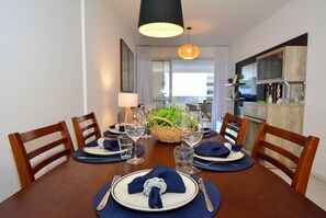 Mesa lista para comer con platos, cubiertos y servilletas, rodeada de sillas de madera.