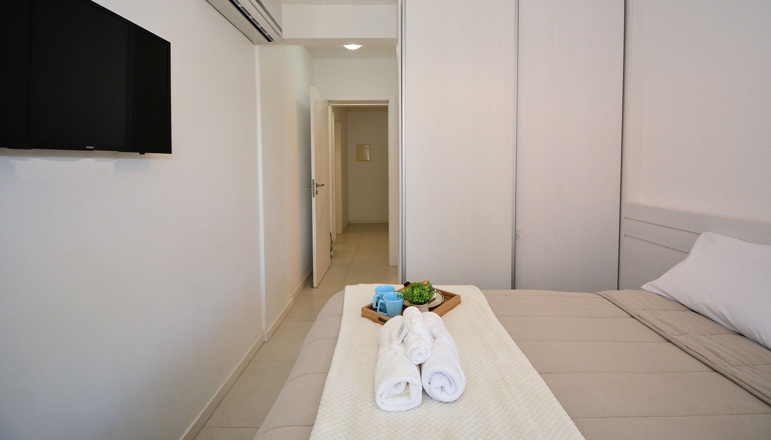 A hotel room with a bed, a TV mounted on the wall, and a tray with towels and a plant.