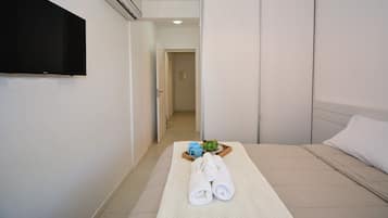 A hotel room with a bed, a TV mounted on the wall, and a tray with towels and a plant.
