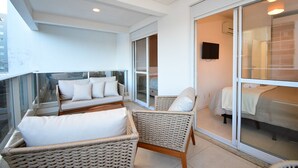 Un balcón con mobiliario de mimbre, un sofá y una cama con un televisor al fondo.
