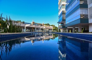 Una piscina con agua azul cristalina, rodeada de edificios modernos con balcones y un cielo despejado.