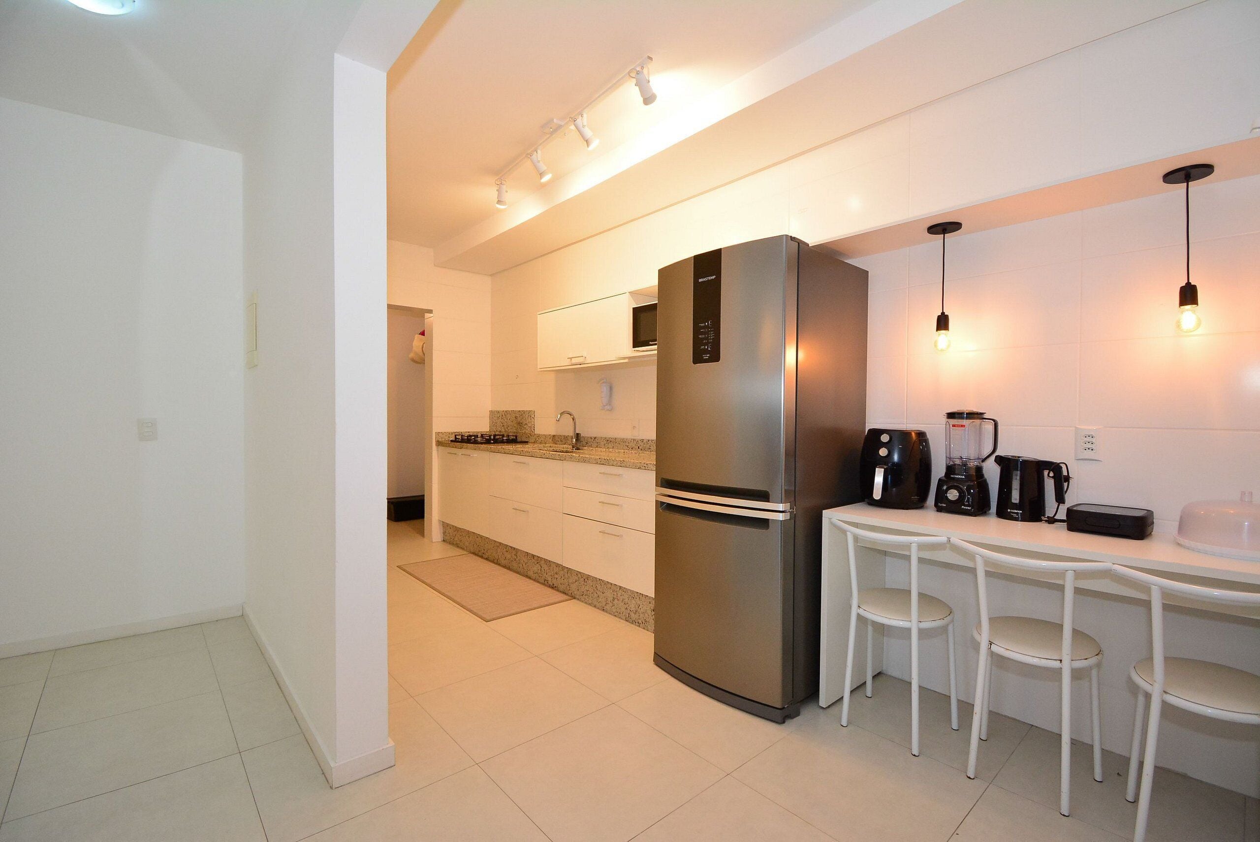 Una cocina moderna con un refrigerador de acero inoxidable, gabinetes blancos y un comedor con dos sillas blancas.