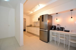 Una cocina moderna con un refrigerador de acero inoxidable, gabinetes blancos y un comedor con dos sillas blancas.