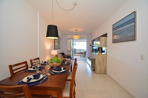 Un comedor con una mesa de madera preparada para cuatro personas, una lámpara colgante y vistas a la cocina.