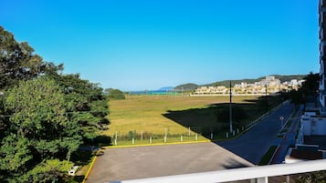 Vista desde un balcón sobre un estacionamiento, con un campo verde y edificios al fondo.
