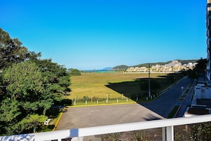 Vista desde un balcón sobre un estacionamiento, con un campo verde y edificios al fondo.