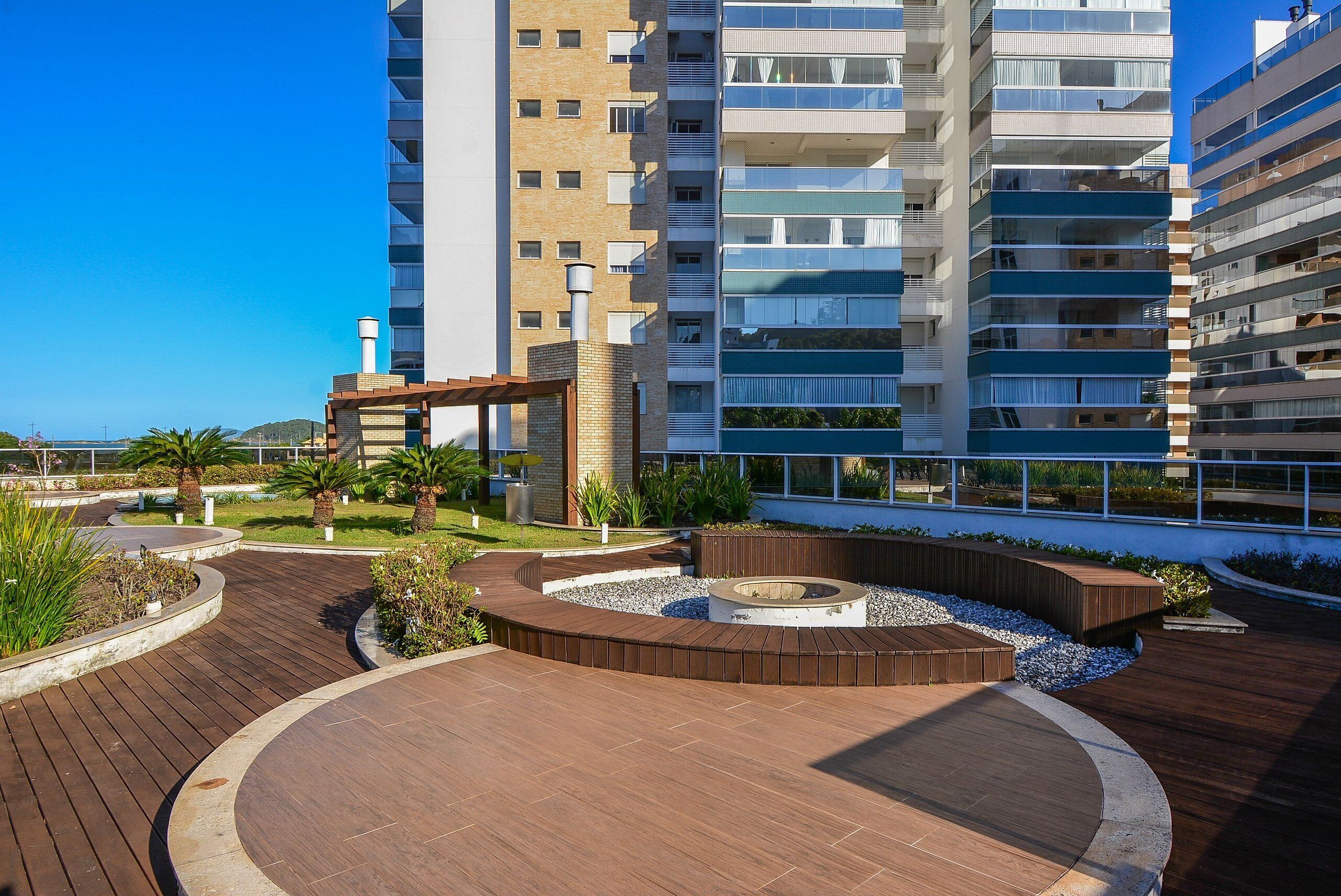 A modern residential building with multiple balconies, a landscaped courtyard with wooden decking, and a fire pit area.