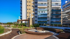 Un edificio residencial moderno con varios balcones, un patio ajardinado con cubierta de madera y una zona con chimenea.