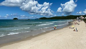 Una playa con cielos despejados, aguas tranquilas y algunas personas disfrutando del sol.