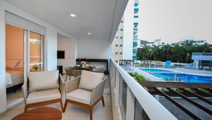 A balcony with wicker chairs, a small table, and a view of a swimming pool and buildings. - Boulevard Praia de Palmas a 400m do Mar (Governador Celso Ramos)