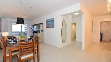 Un comedor moderno con una mesa de madera preparada para cuatro personas, una lámpara colgante y una cocina al fondo.
