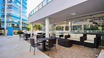 An outdoor seating area with wicker furniture and a glass railing overlooking a modern building.