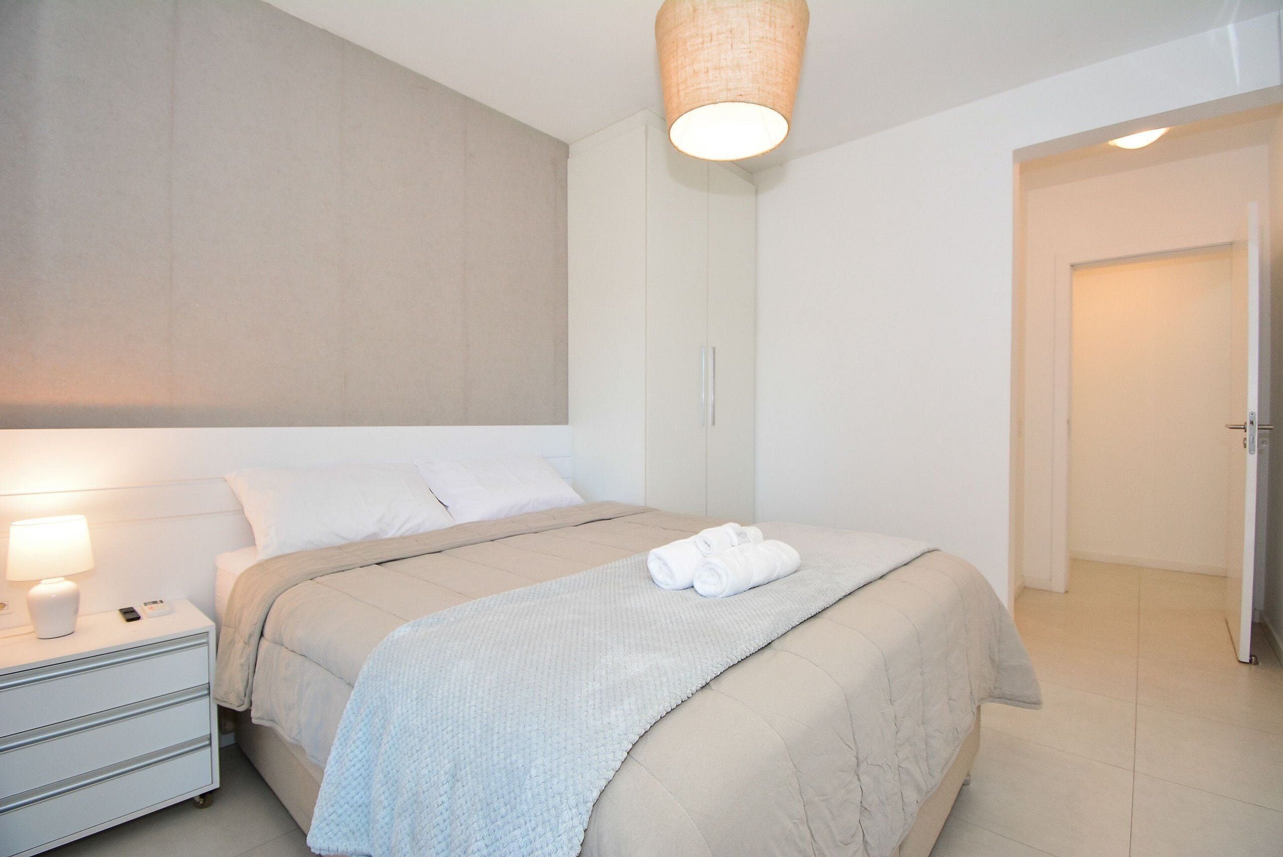 Un dormitorio moderno con cama, mesita de noche y lámpara colgante.