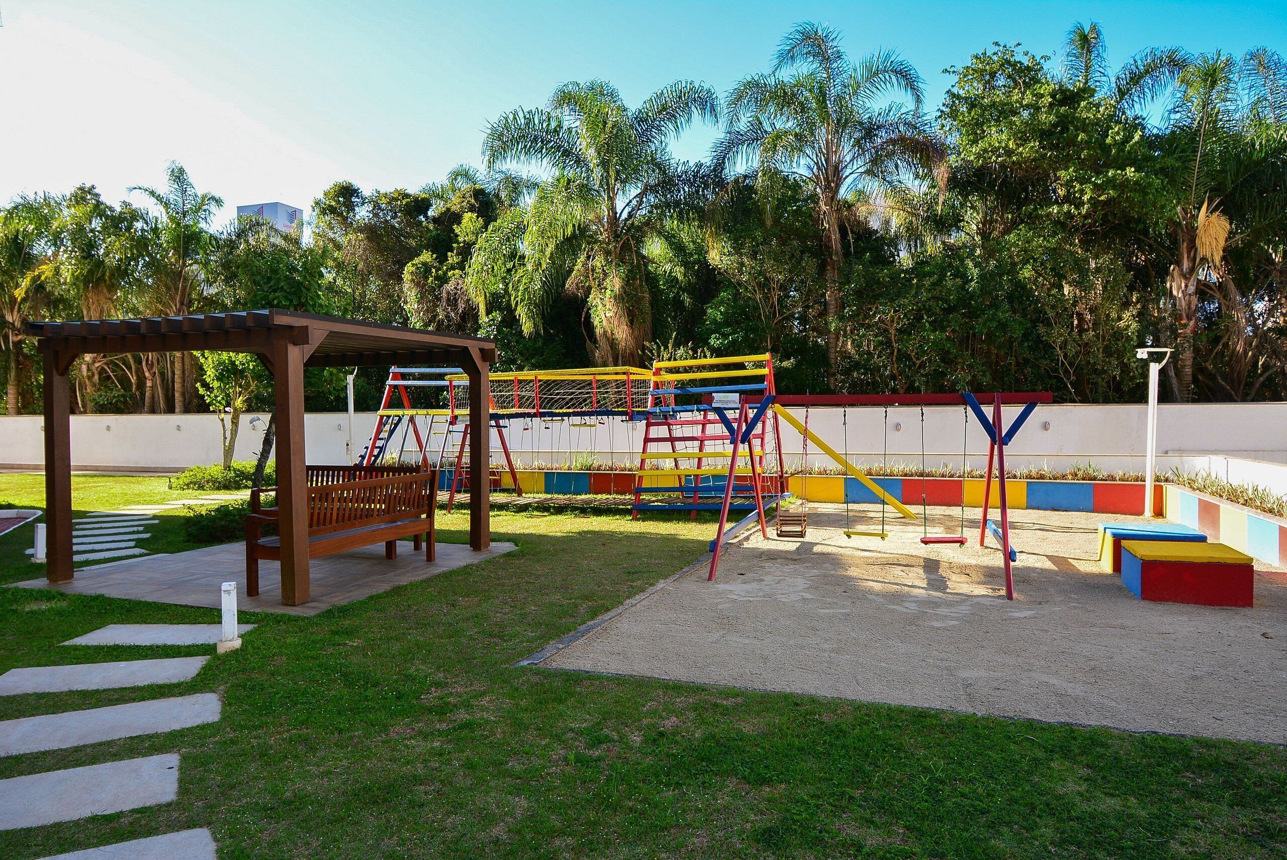 Un parque infantil con un banco de madera, columpios y una estructura para escalar.