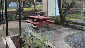 Een overdekt terras met een houten tafel en bankjes, omringd door potplanten en een stenen muur.