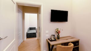 A hotel room with a wooden desk, a chair, a flat-screen TV mounted on the wall, a small table with a vase of flowers, and a sofa in the background. - Hotel Settefiori (Florence)