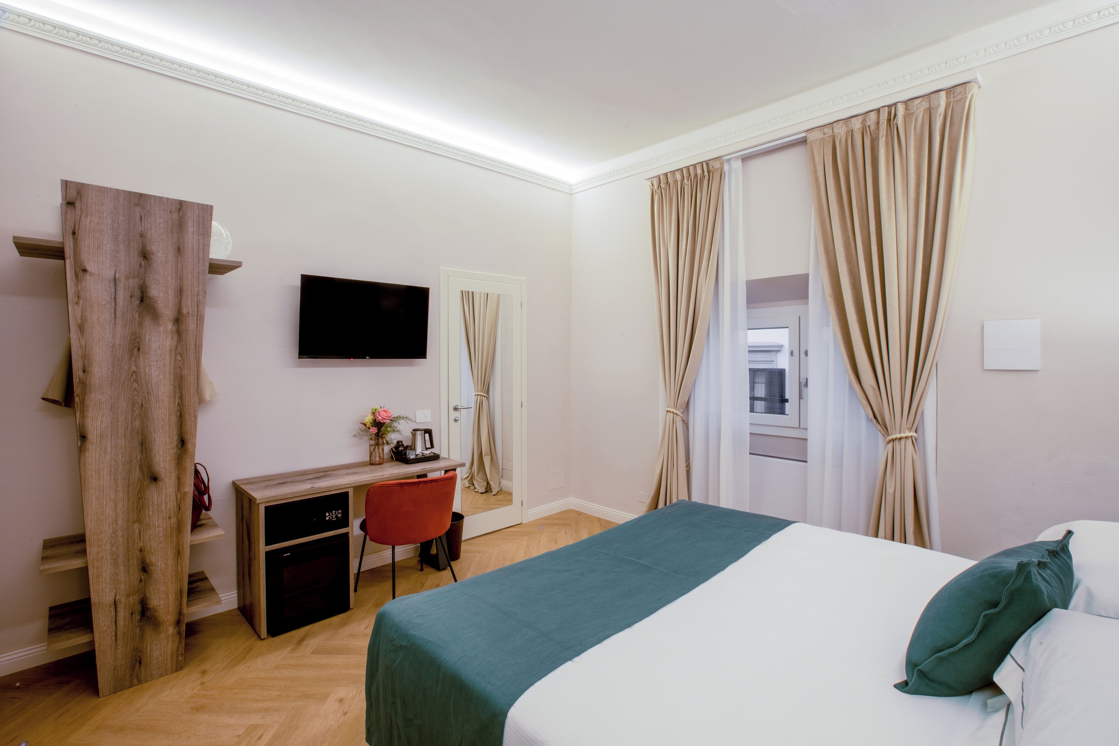 Una habitación de hotel con cama, escritorio, silla, televisor y cortinas.