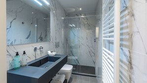 A modern bathroom with a large mirror, a black vanity, a glass shower enclosure, and marble walls. - Hotel Settefiori (Florence)