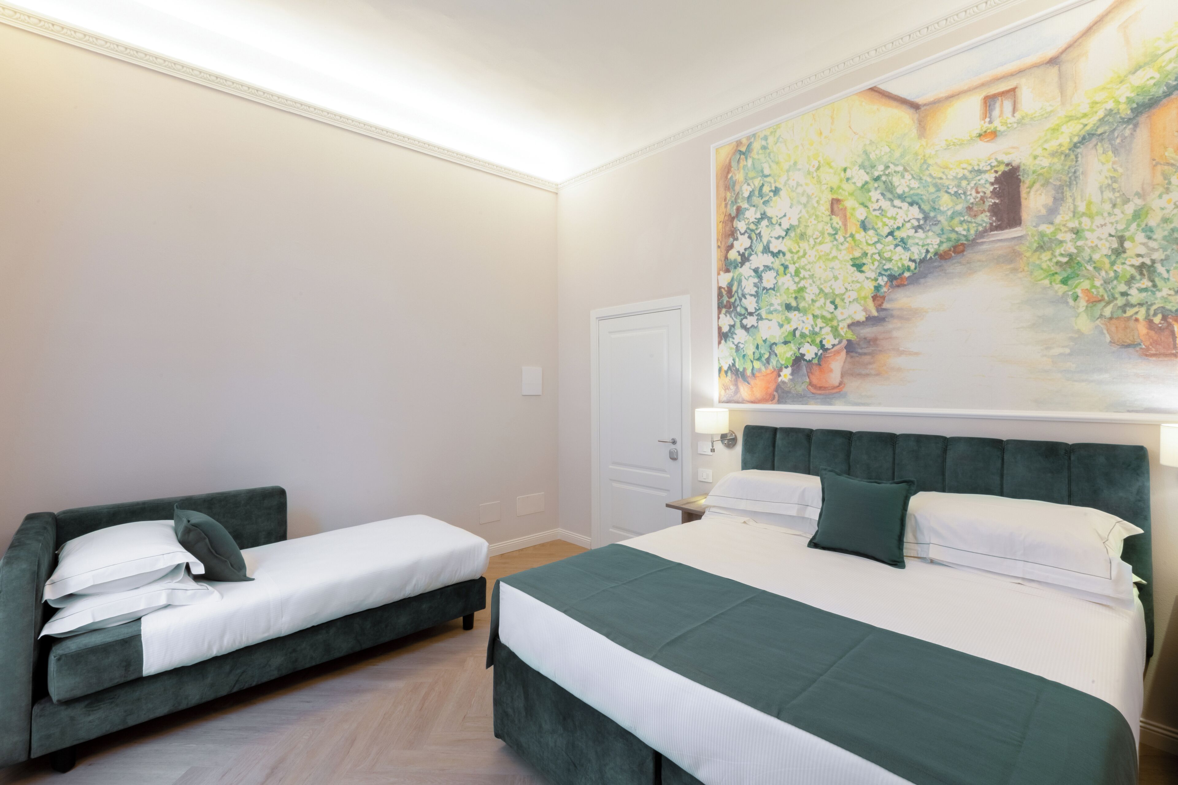 A hotel room with a bed, a sofa, and a painting of a garden on the wall.