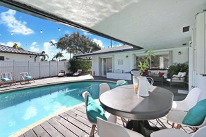 Un espace aménagé au bord de la piscine, avec une table et des chaises, un patio couvert et une vue sur le jardin.