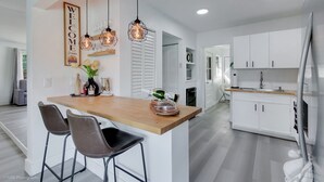 Uma cozinha moderna com uma ilha de madeira, luminárias pendentes e um letreiro com a mensagem 'WELCOME Home'.