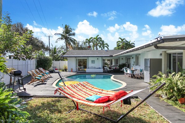 Un jardin avec une piscine, des chaises longues, un hamac et une terrasse.