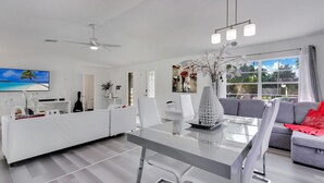 Uma sala de estar moderna com uma mesa de jantar de vidro, sofás brancos e um ventilador de teto.