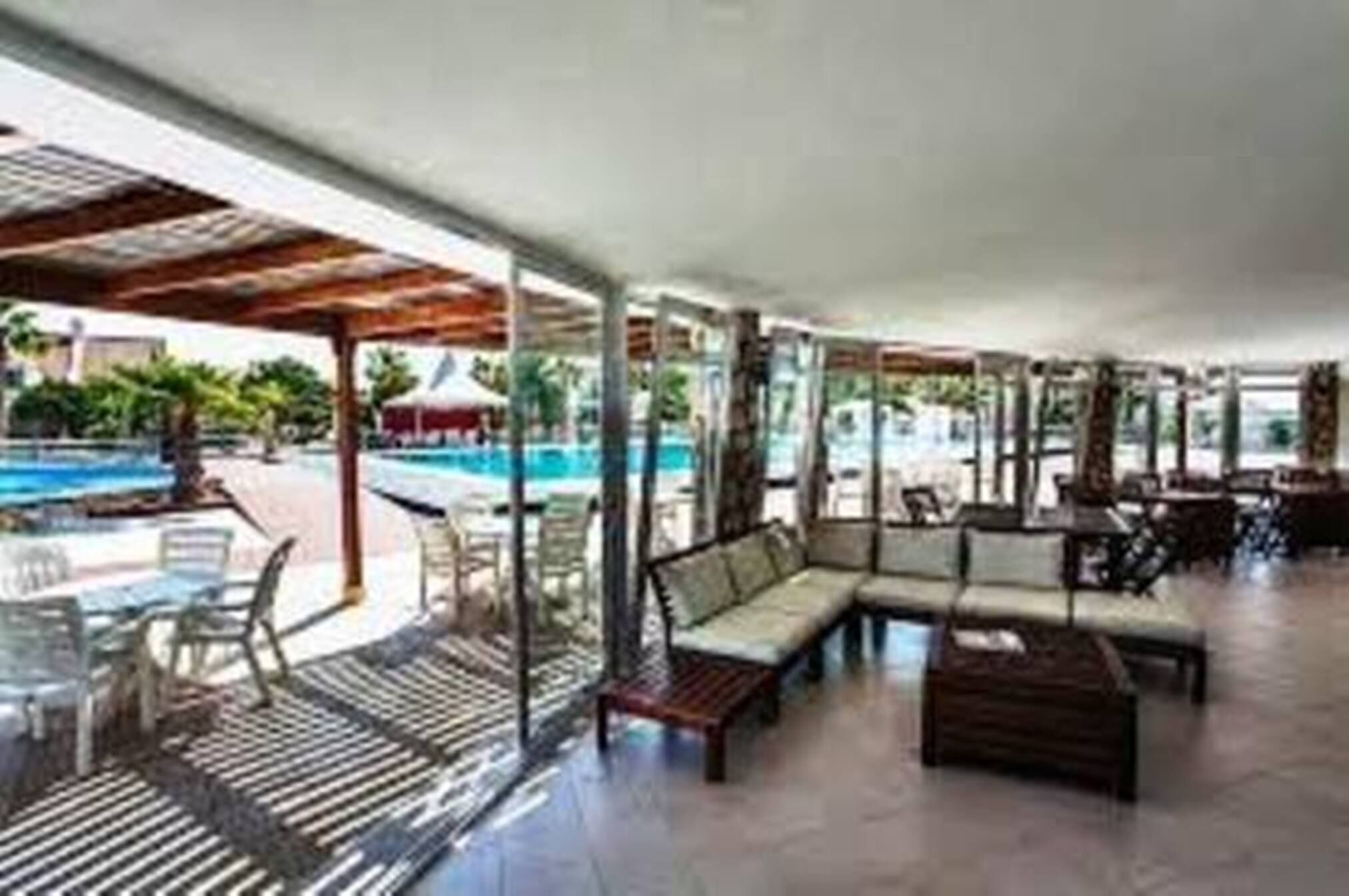 Un área de estar al aire libre techada, con piscina, sillones de descanso y mesas.