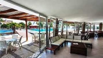 Un área de estar al aire libre techada, con piscina, sillones de descanso y mesas.