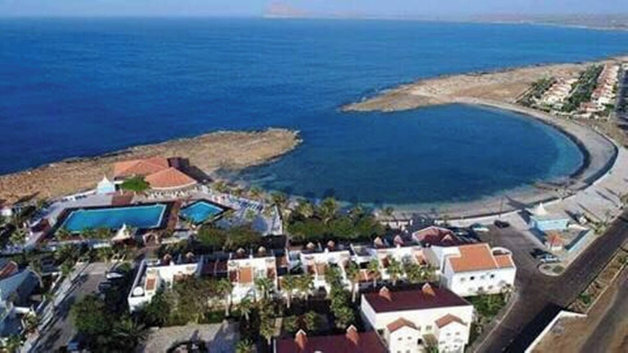 Ein Luftbild eines Küstenresorts mit mehreren Schwimmbecken, Strandvillen und einem Sandstrand.