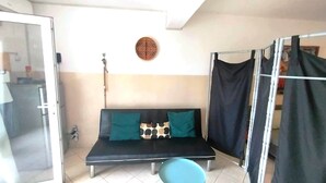 A room with a black sofa, teal cushions, a patterned wall hanging, and a metal rack. - Studio Murdeira Side Beach Ecologic Protected Bay, Snorkling include, Pool (Ilha do sal)