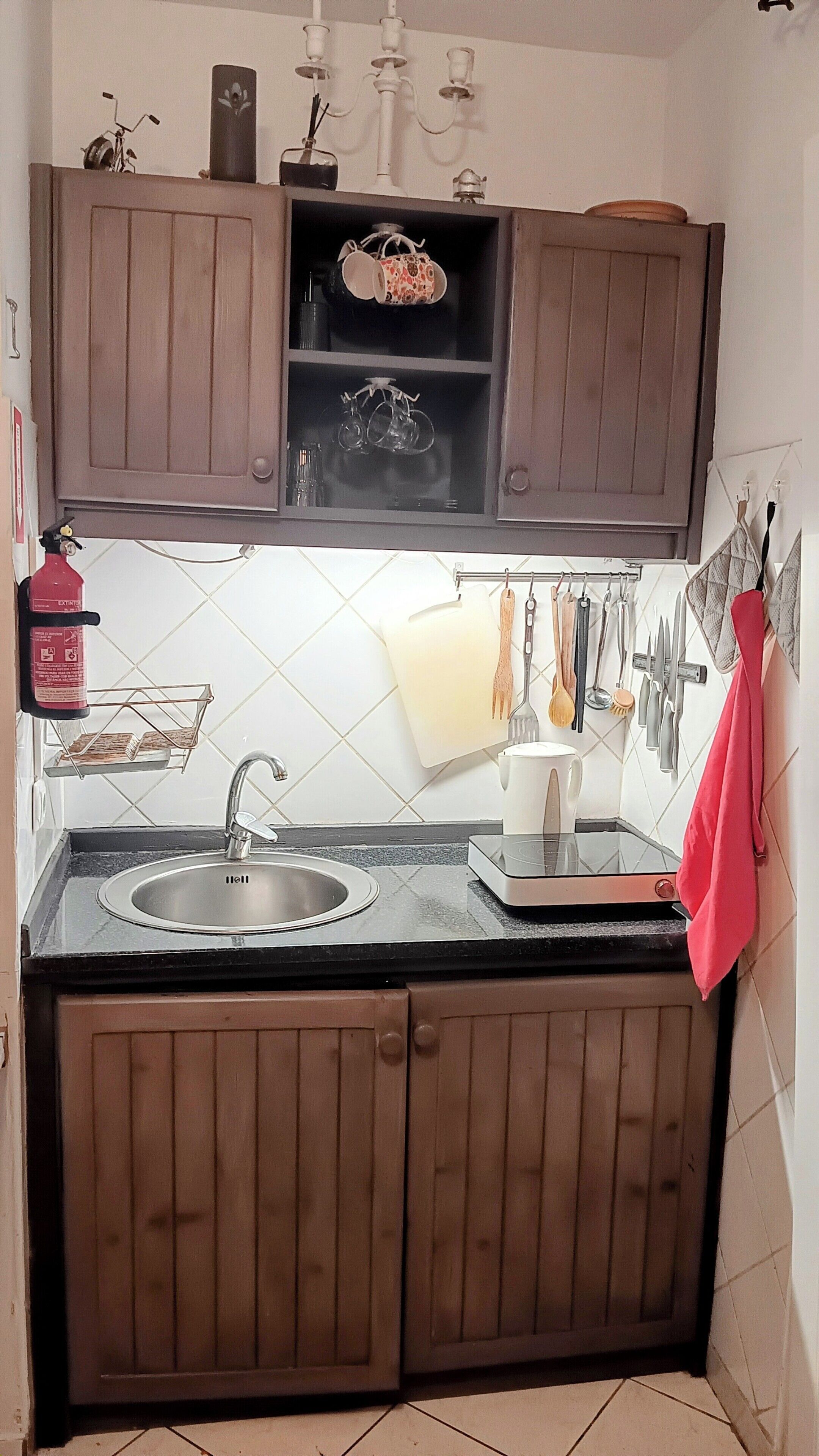 Una cocina con armarios de madera, un fregadero y varios utensilios colgados en la pared.