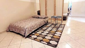 A small, neatly arranged bedroom with a bed, a small table, and a patterned rug. - Studio Murdeira Side Beach Ecologic Protected Bay, Snorkling include, Pool (Ilha do sal)