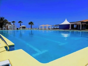A swimming pool with clear blue water, surrounded by palm trees and a white tent structure.