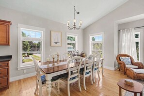 A dining area with a wooden table, white chairs, and a chandelier. - 5-Min to South Beach | Golf Cart, Hot Tub & Arcade (South Haven)