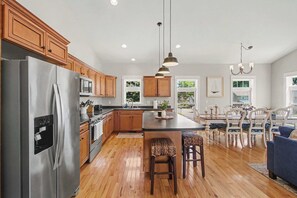 Une cuisine moderne dotée d’appareils électroménagers en acier inoxydable, de meubles en bois, d’un îlot central et d’un coin repas agrémenté d’un lustre.