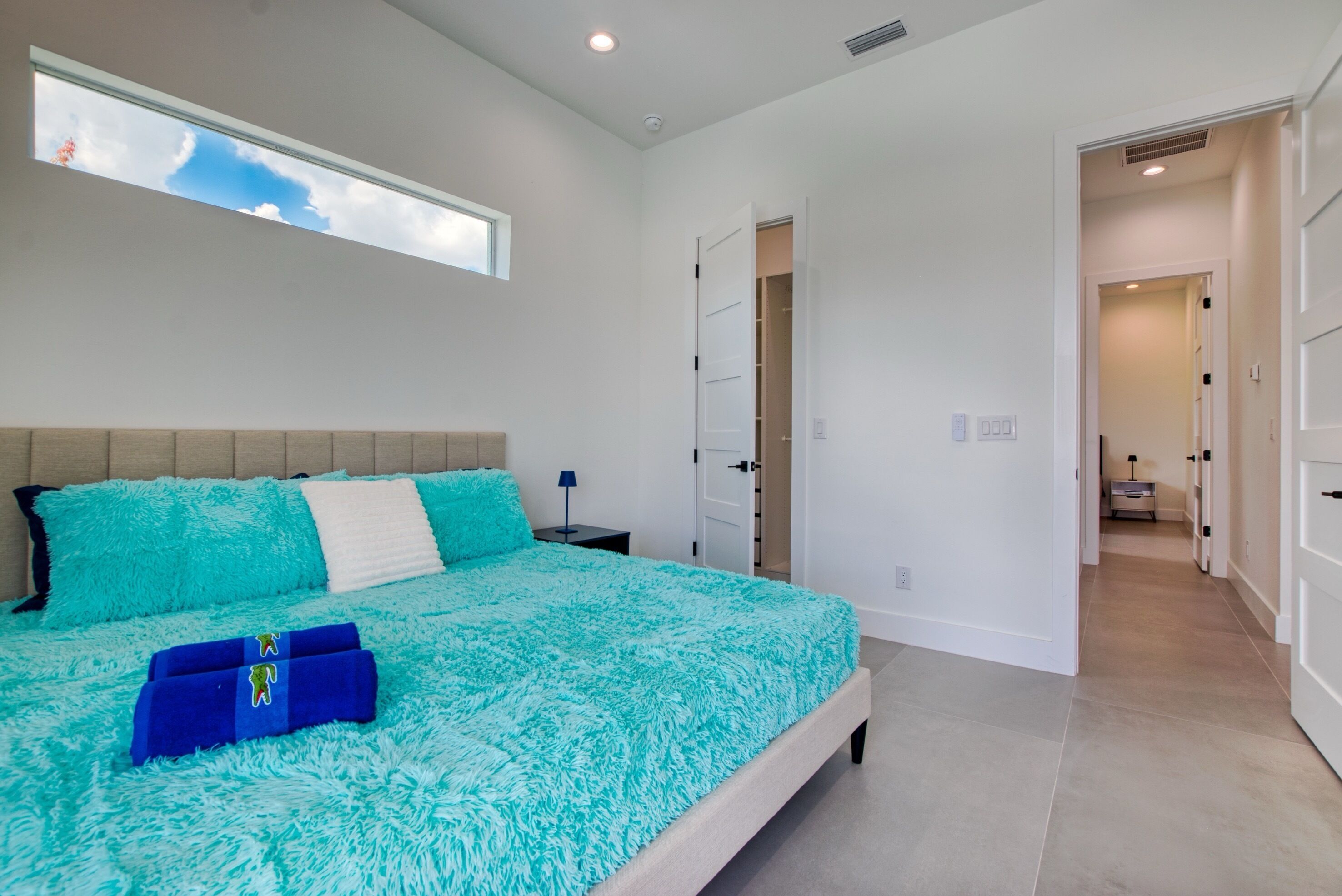 A bedroom with a large bed, a window, and a hallway leading to another room.
