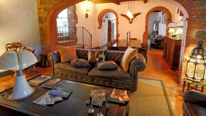 Una sala de estar acogedora con un sofá de cuero, una mesa de centro con libros y una lámpara, y un arco de ladrillo que conduce a otra habitación.
