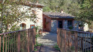 Un edificio rústico de piedra con techo de tejas, un sendero de grava y una valla metálica.